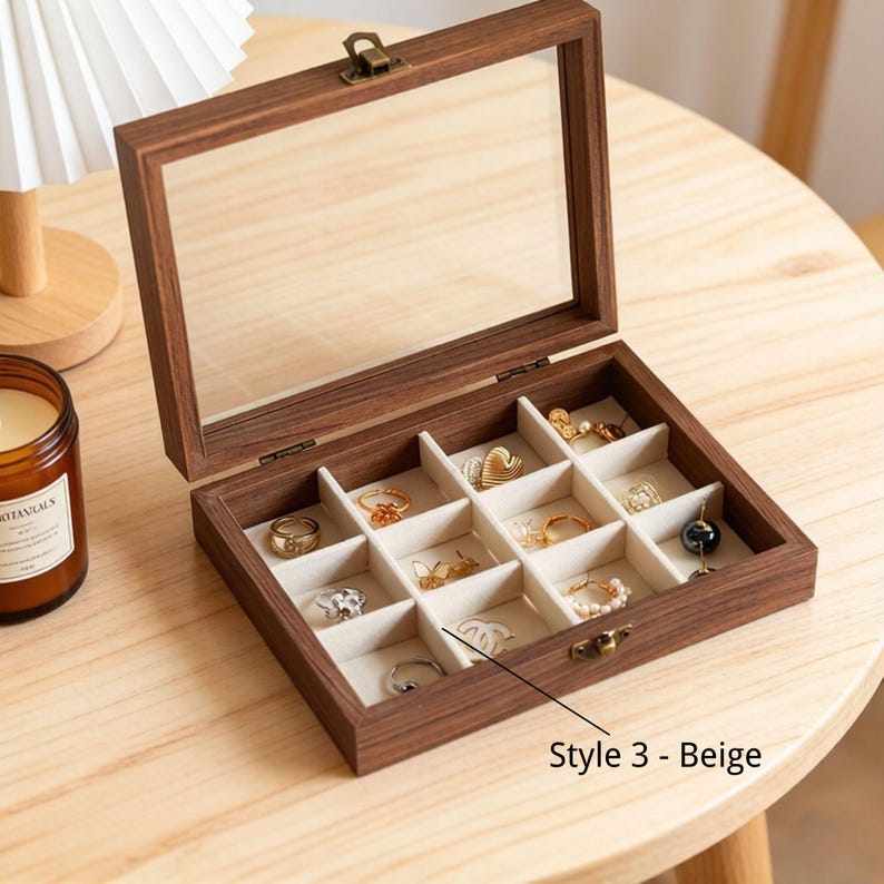 K&ouml;nnte beinhalten: Ge&ouml;ffnete Schmuckschatulle aus Holz mit Glasdeckel, die verschiedene Ringe in einzelnen F&auml;chern zeigt. Die Box ist braun mit beigem Innenraum und einem Messingverschluss. Der Text "Style 3 - Beige" ist sichtbar.