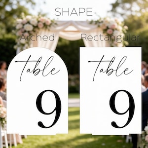 May include: Two white table number signs with black text. One sign is arched and the other is rectangular. Both signs feature the word Table in a script font above the large number 9 in a serif font. The word SHAPE is centered above them.