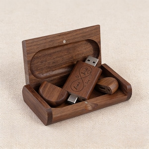 May include: A wooden USB flash drive with an infinity symbol design, engraved with the names "Anna & Jordi" and the date "10 July 2017". The drive is inside a matching wooden box with a magnetic closure. The box also contains a USB port cover.