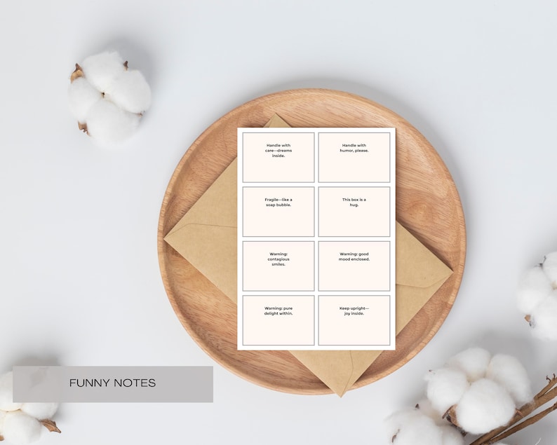 Pu&ograve; includere: Un set di otto biglietti color crema con frasi umoristiche, presentato su un piatto di legno con una busta marrone. Il testo include frasi come "Handle with care - dreams inside" e "This box is a hug."