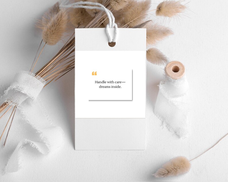 Pu&ograve; includere: Un'etichetta regalo bianca con un cordino, con il testo "Handle with care&mdash;dreams inside." L'etichetta &egrave; ambientata su uno sfondo di fiori secchi, nastro bianco e una bobina di legno, creando un'estetica minimalista.