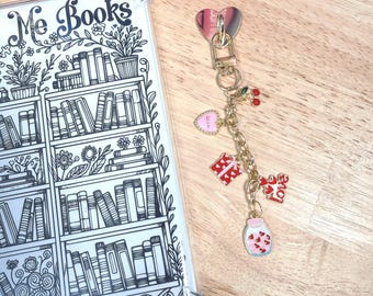 Könnte beinhalten: Eine transparente Handyhülle mit einem schwarz-weißen Bücherregal-Design und den Worten "Me Books". Ein goldener Schlüsselanhänger mit Herz-, Kirsch- und Geschenk-Anhängern ist befestigt.