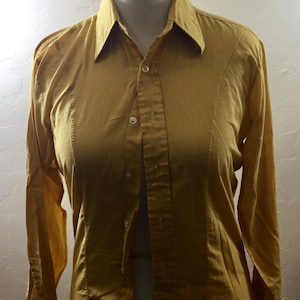May include: A long-sleeved button-down shirt in a mustard yellow color with thin red stripes. The shirt has a classic collar and a button-up front.