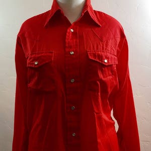 May include: A red long-sleeved button-down shirt with two chest pockets and silver buttons.