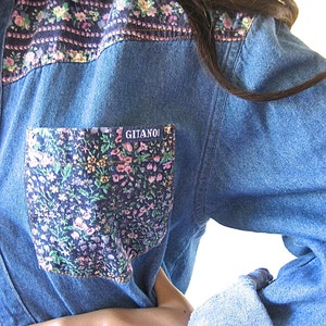 May include: A blue denim shirt with a floral print on the collar and a pocket. The pocket has a floral print and the word "GITANO" in white letters.