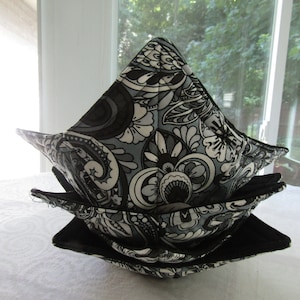 May include: A stack of three square fabric bowls. The bowls feature a black, white, and gray floral pattern on the exterior and a solid black interior. The bowls are stacked on top of each other.