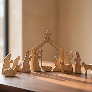 Puede incluir: Escena de la Natividad de madera con figuras de la Sagrada Familia, ángeles y animales. Las figuras son de madera clara y están dispuestas sobre una superficie de madera. Una estrella está encima del establo.
