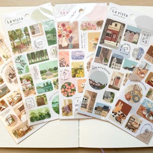 以下が含まれることがあります： 風景、建物、花の配置など、さまざまな水彩イラストが描かれた5枚のステッカーシート。「La vista」とラベル付けされ、さまざまな小さな装飾ステッカーが特徴です。白いノートに配置されています。