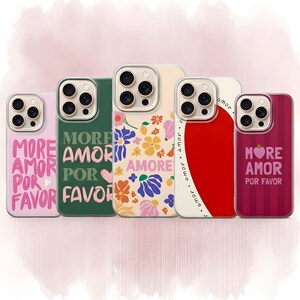 Op de afbeelding: Vijf telefoonhoesjes met verschillende ontwerpen en de tekst "More Amor Por Favor". De hoesjes hebben bloemenpatronen, een rood hart en een gestreept ontwerp. De hoesjes zijn in roze, groen, crème en rood.