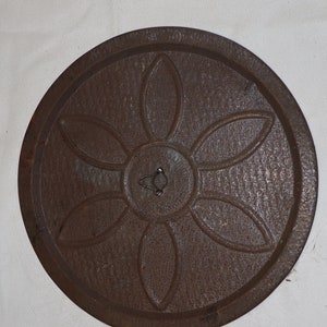 May include: A round, wooden, brown tray with a carved flower design in the center. The tray has a small metal ring in the center.