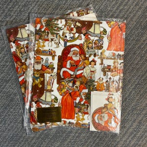 May include: Two sheets of Christmas wrapping paper and a matching gift tag enclosed in clear plastic packaging. The paper features a detailed, colorful illustration of Santa Claus, children, toys, and holiday decorations on a white background.