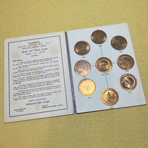 May include: A collection of Wildwood Elks Lodge medals and tokens from 1965 to 1972, displayed in a booklet. The booklet includes text about the medals and their history. The medals are bronze and nickel-silver, each approximately 1.5 inches in diameter.