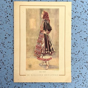 May include: A vintage print of a woman in traditional Greek Thracian attire. The woman is wearing a black jacket, a patterned skirt, and a red headscarf. The print has a beige border and text in Greek.