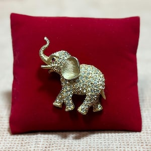 May include: A gold-toned elephant brooch with clear rhinestones and a single red rhinestone for an eye.