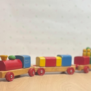 May include: A wooden toy train with a red engine, blue, yellow, and red boxcars, and a green and yellow caboose. The train is on a wooden surface.