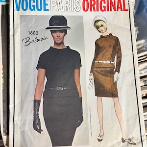 May include: Vogue Paris Original sewing pattern number 1682 for a Balmain design. The pattern features two illustrations of women wearing dresses. One woman is wearing a black dress with a black hat and the other is wearing a brown dress with a white hat.
