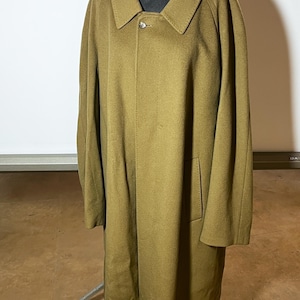 May include: A long, olive-green wool coat featuring a classic fold-down collar, long sleeves, and a single visible button closure at the neckline. The coat has a straight, structured silhouette with two side pockets and a smooth, solid-colored finish.