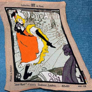 May include: Needlepoint tapestry featuring the "Jane Avril" poster by Toulouse-Lautrec. The artwork depicts a woman in a yellow dress and orange coat. The tapestry is labeled "Collection de Paris" and "Made in France". The dimensions are 60x80.