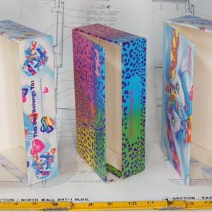 May include: Three rectangular cardboard boxes with hinged lids. Two boxes feature a blue sky background with unicorn illustrations, rainbow hearts, and the text This Box Belongs To. The center box has a vibrant rainbow leopard print pattern.
