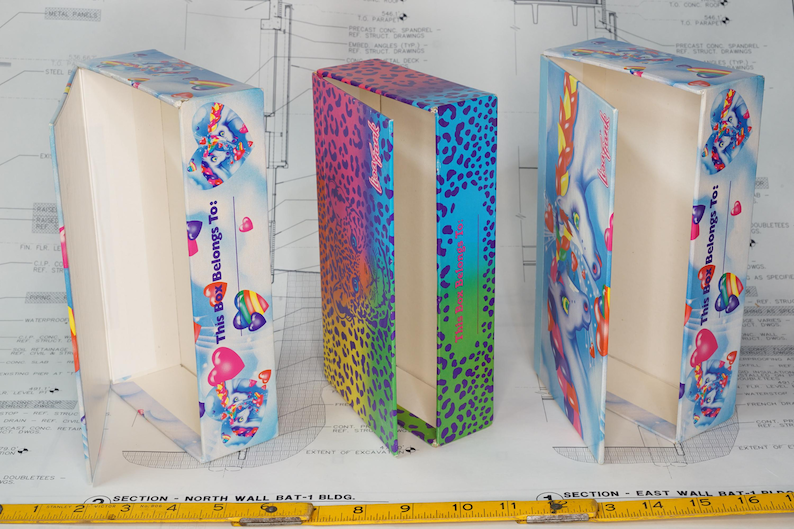 May include: Three rectangular cardboard boxes with hinged lids. Two boxes feature a blue sky background with unicorn illustrations, rainbow hearts, and the text This Box Belongs To. The center box has a vibrant rainbow leopard print pattern.