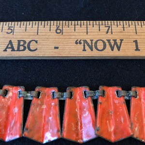 May include: A close-up of a red and silver metal chain necklace. The necklace is made up of a series of small, rectangular, red enamel pieces connected by silver metal links. The necklace is about 6 inches long.