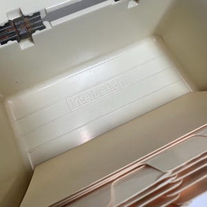 May include: A beige plastic file box with the "InterDesign" logo. The box has a ridged interior and a hinged lid. The text "MADE IN USA" is visible.