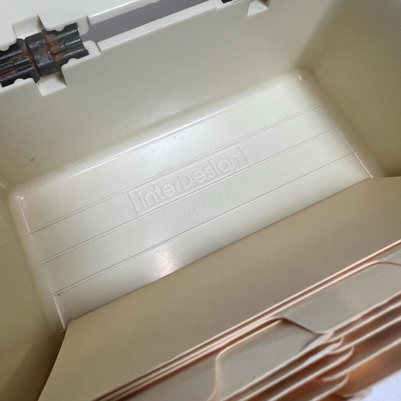 May include: A beige plastic file box with the "InterDesign" logo. The box has a ridged interior and a hinged lid. The text "MADE IN USA" is visible.