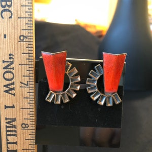 May include: A pair of earrings with a silver-toned circular design and a red, rectangular stone in the center.