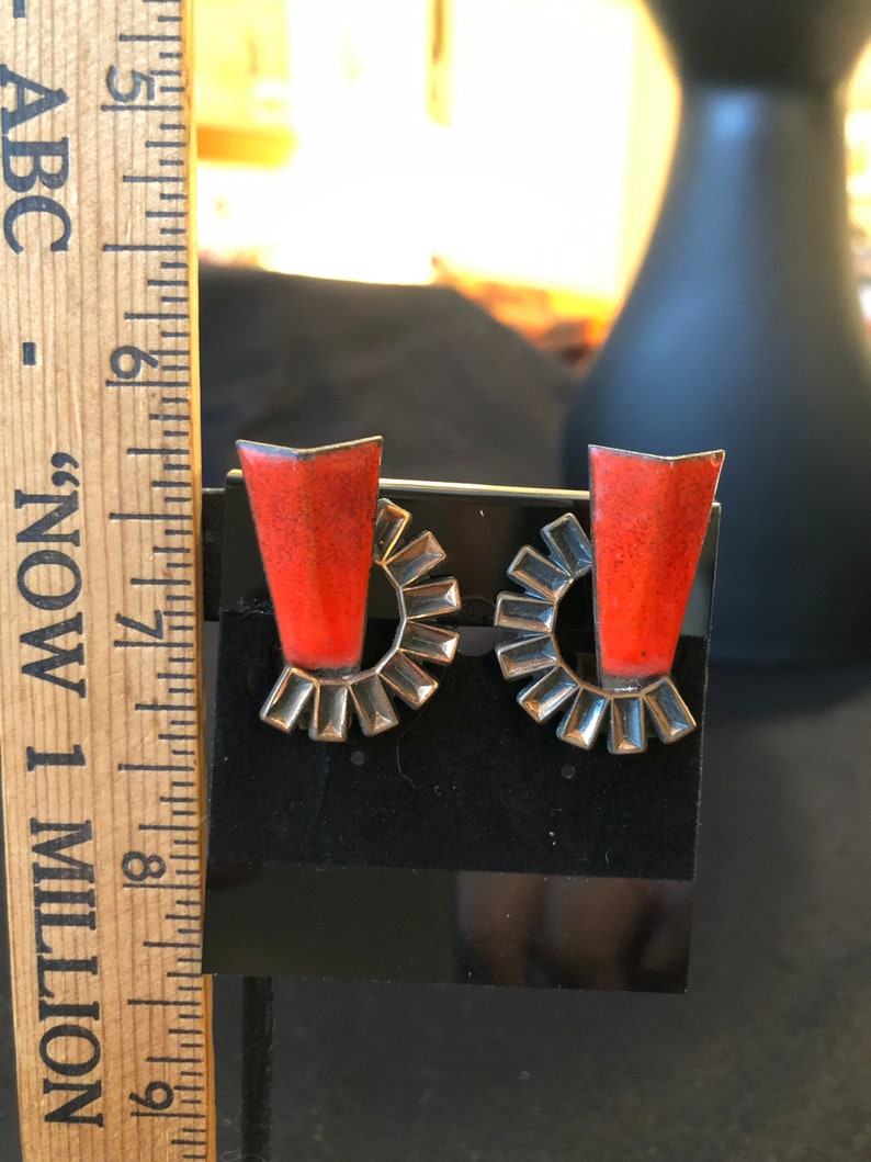 May include: A pair of earrings with a silver-toned circular design and a red, rectangular stone in the center.
