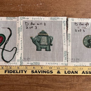 May include: Three needlepoint canvases with hand-stitched designs. The first canvas features a heart with a watermelon pattern. The second canvas shows a teapot. The third canvas displays a teacup and saucer. Each canvas has the text "D for all 3" and "1 of 3", "2 of 3", and "3 of 3".