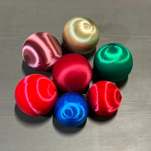 May include: Seven satin Christmas ornaments in various colors, including red, green, blue, gold, and pink. The ornaments have a swirl pattern.