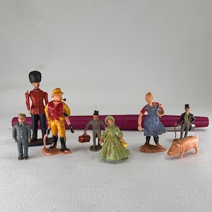 May include: A collection of miniature figurines depicting various figures, including a soldier, hunter, and woman in a green dress. The figurines are painted in vibrant colors and are set against a white background.