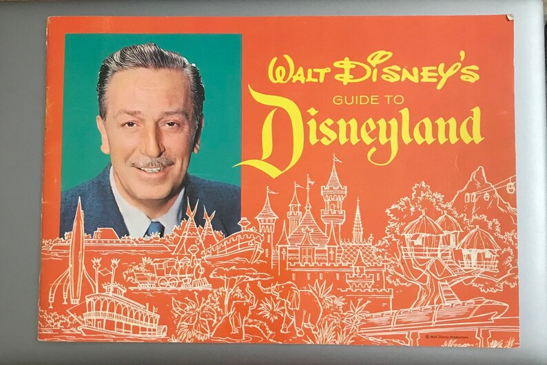 Puede incluir: Una gu&iacute;a vintage naranja y amarilla para Disneyland con un retrato de Walt Disney e ilustraciones de las atracciones del parque. El texto dice "Walt Disney's Guide to Disneyland".