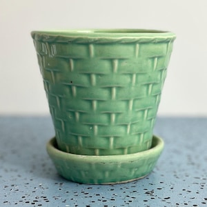 May include: A light green ceramic planter with a basket weave design. The planter has a matching saucer. The planter is approximately 5 inches tall and 5 inches wide.