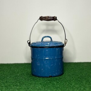 May include: A cylindrical blue enamel bucket with a mottled white pattern, featuring a matching lid with a small handle, a metal wire bail handle, and a dark brown wooden grip centered on the top of the wire handle for carrying purposes.