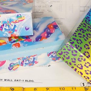 May include: Three rectangular boxes with colorful designs. Two boxes feature a light blue background with white unicorns, rainbow hearts, and red hearts. The third box has a vibrant rainbow gradient background with a purple leopard print pattern.