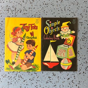 May include: Two vintage coloring books. The yellow cover reads "Tiny Tots Coloring Book" with illustrations of children and a butterfly. The black cover says "Simple Objects Coloring Book" with a clown and sailboat illustration.