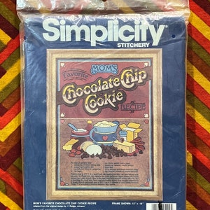 May include: A cross-stitch kit featuring a vintage-style illustration of a chocolate chip cookie recipe. The kit includes 100% wool crewel yarn, cotton floss, needles, an instruction sheet, and a stitch chart. The frame is not included. The kit is made in the USA.