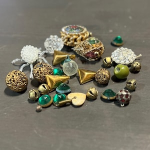 May include: Assortment of decorative beads and charms in gold, green, and white. The beads are made of glass, metal, and plastic. Some of the beads are shaped like bells, stars, and hearts.