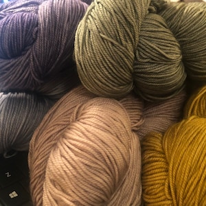 May include: Four skeins of yarn in different colors: purple, green, beige, and yellow. The yarn is soft and fluffy, perfect for knitting or crocheting.