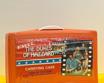 Può includere: Una valigetta di trasporto in plastica arancione per auto in miniatura in metallo pressofuso. La valigetta è dotata di una maniglia bianca, una bandiera americana rossa, bianca e blu e il testo "ERTL The Dukes of Hazzard Carrying Case Holds 24 1/64 Scale ERTL Die-Cast Miniature Cars."
