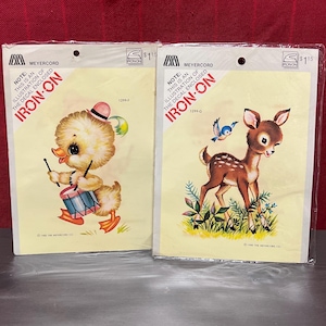 May include: Two vintage iron-on transfer sheets featuring a yellow duck playing a drum and a brown deer with a blue bird. The sheets are packaged together and have the text "Iron-On" and "1299 F" and "1299 G" printed on them.