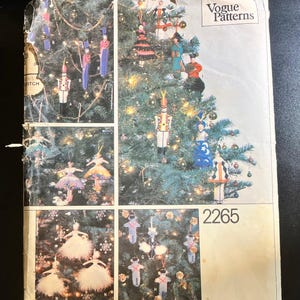 May include: A vintage Vogue Patterns sewing pattern featuring a Christmas tree decorated with various ornaments. The ornaments include ballerina figures, soldiers, and other festive designs. The pattern number 2265 is visible.