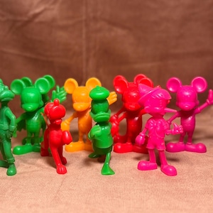 May include: A collection of nine vintage plastic figurines, including Mickey Mouse, Donald Duck, and Goofy. The figurines are in various colors, including green, red, yellow, and pink.