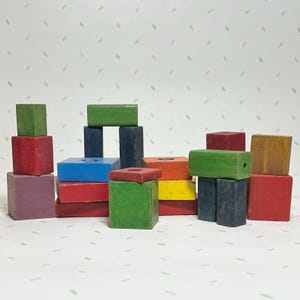 May include: A collection of colorful wooden blocks in various shapes and sizes. The blocks are painted in shades of red, green, blue, yellow, orange, and purple. Some blocks are stacked, creating a playful arrangement. A classic toy for creative play.