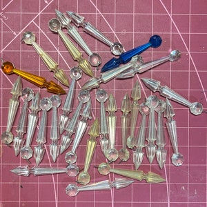 May include: A collection of clear glass crystal prisms with a variety of shapes and sizes. The prisms are arranged on a pink cutting mat.