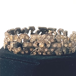 May include: A silver bracelet with a geometric design and clear rhinestones. The bracelet is on a black velvet display box.