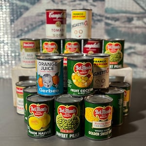 May include: A collection of canned goods, including Del Monte brand fruit cocktail, peach halves, and sweet peas, as well as Gerber baby food, Franco-American Spaghetti, and Campbell's Tomato Soup.