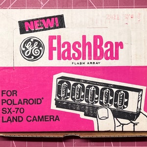 May include: A pink box with a white label that says "NEW!" and "GE FlashBar Flash Array" with a black and white illustration of the flash bar. The box says "FOR POLAROID SX-70 LAND CAMERA".