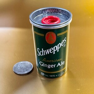 May include: A miniature replica of a Schweppes American Ginger Ale can. The can is green with gold lettering and a red cap. The can is labeled "Schweppes American Ginger Ale" and "No. 1870 W. Germany".